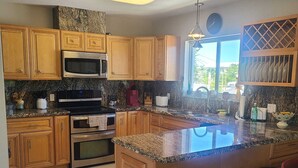 A modern kitchen with wooden cabinets, stainless steel appliances, a granite countertop, and a large island with bar stools. - Waterfront private Key Largo Oasis House, with a Boat Dock (Key Largo)