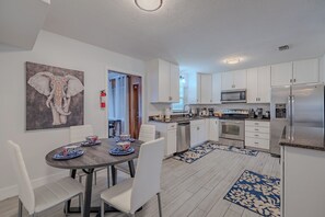 A modern kitchen with white cabinets, stainless steel appliances, and a dining area with a round table and chairs.