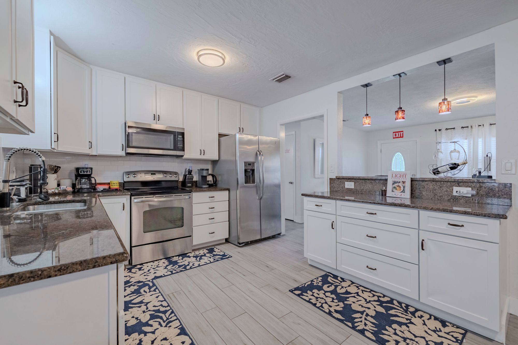 A modern kitchen with white cabinets, stainless steel appliances, granite countertops, and a patterned rug.