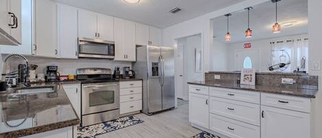 A modern kitchen with white cabinets, stainless steel appliances, granite countertops, and a patterned rug.