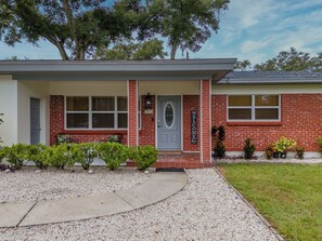 A two-story house with a red brick facade, a grey door, and a welcome sign.