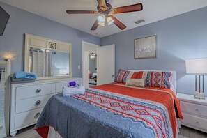 Une chambre à coucher comprenant un lit, une commode, un miroir, un ventilateur de plafond et des œuvres d’art accrochées au mur.