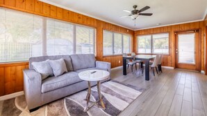 Une pièce spacieuse avec un canapé gris, une table ronde et un ventilateur de plafond.