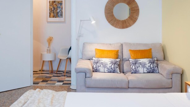 A modern living room with a sofa, two pillows, a round mirror, and a framed artwork on the wall. - Flora Cozy Flat close to Metro (ROMA)