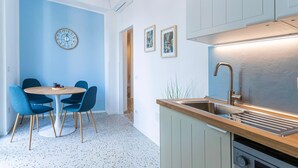 A modern kitchen with a stainless steel sink, wooden countertop, and a round dining table with blue chairs. - Flora Cozy Flat close to Metro (ROMA)