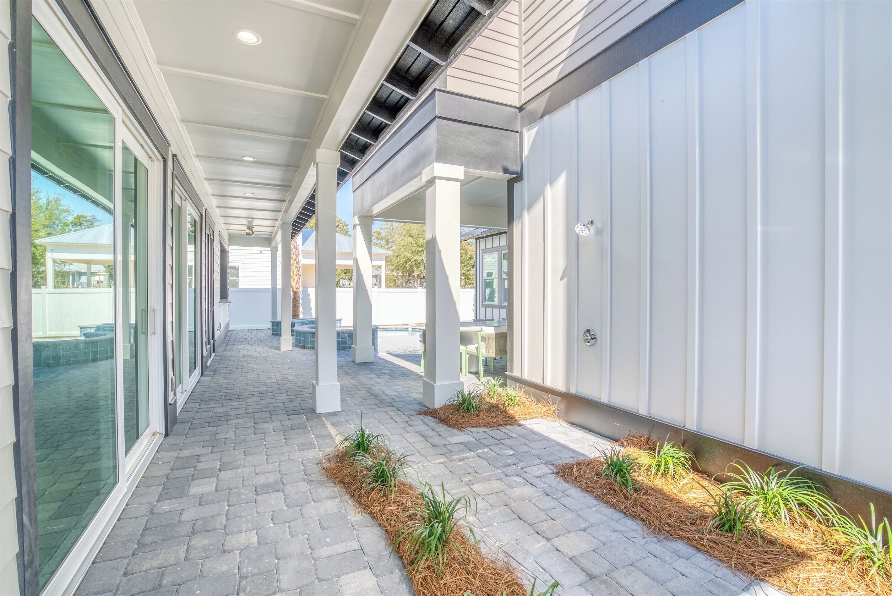 A covered walkway with a brick floor, white pillars, and small plants along the sides.
