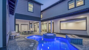 Ein Schwimmbecken mit Whirlpool, eine Terrassenanlage mit Gartenmöbeln sowie ein Gebäude mit zahlreichen Fenstern und Türen.
