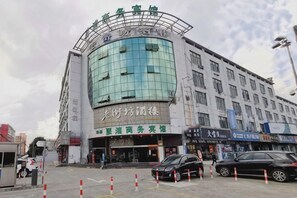 A multi-story building with a curved glass facade, signage for a hotel and a business center, and several parked cars.