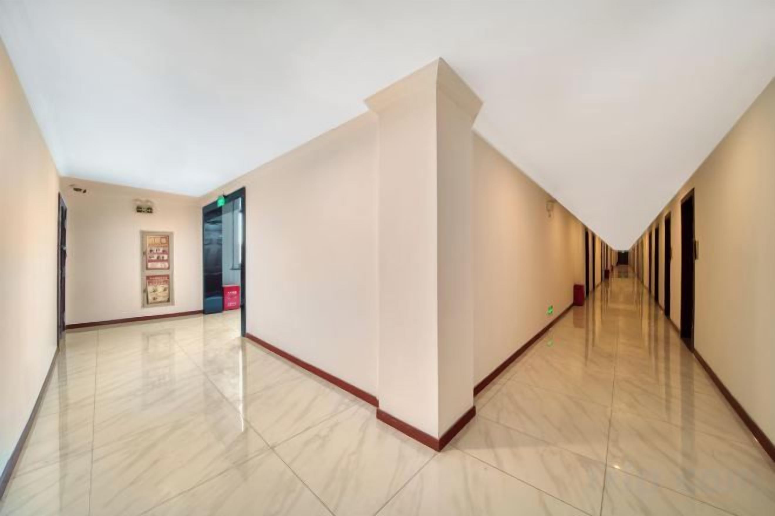 Corredor de hotel com piso lustroso, uma porta à esquerda e um letreiro fixado na parede.