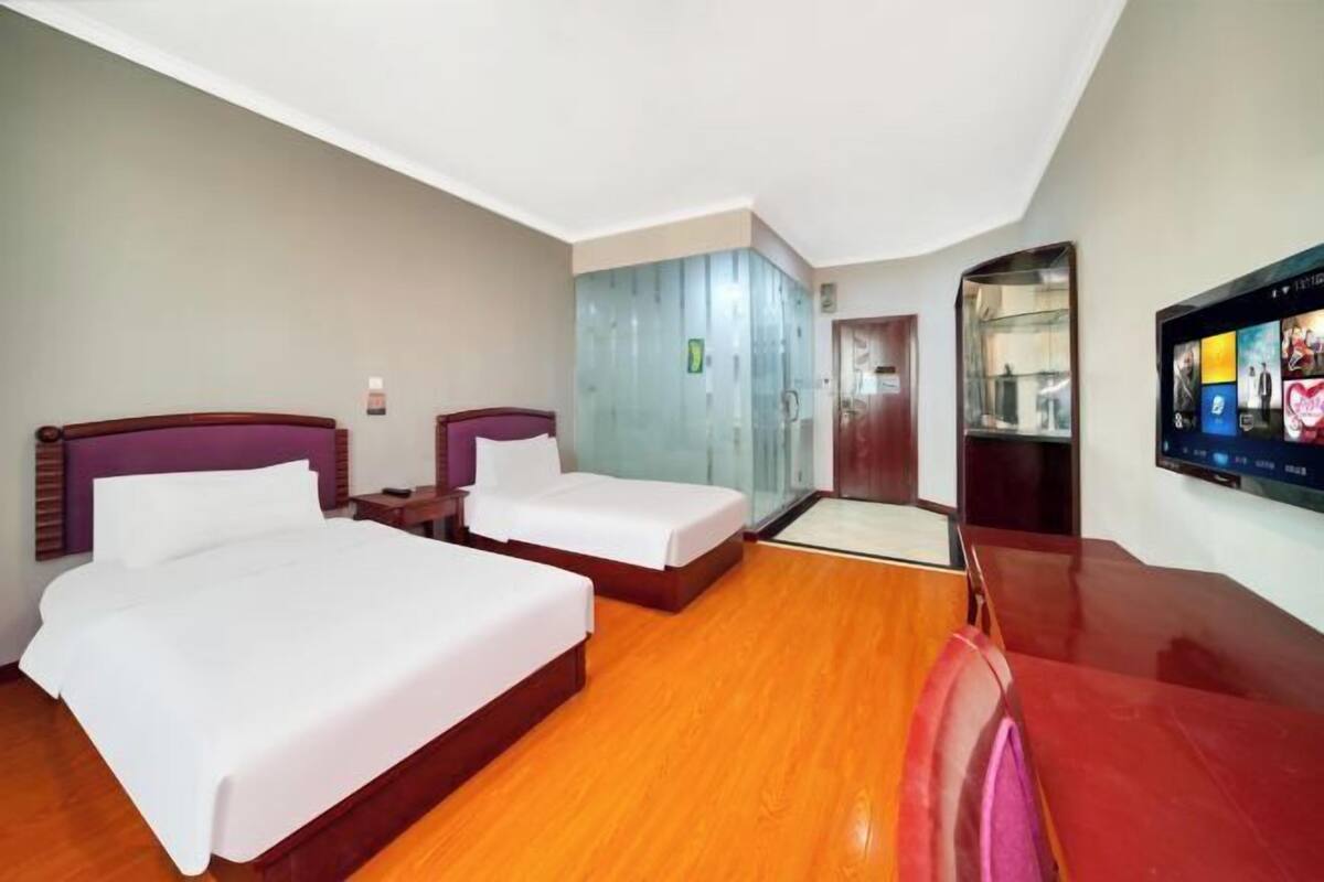 A hotel room with two beds, a TV, a wardrobe, and a mirror.