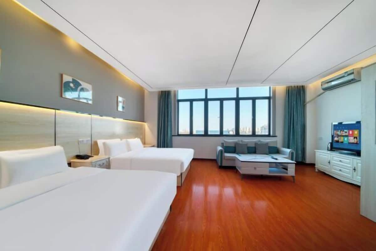 A hotel room with two beds, a sofa, a TV, and a large window with a city view.
