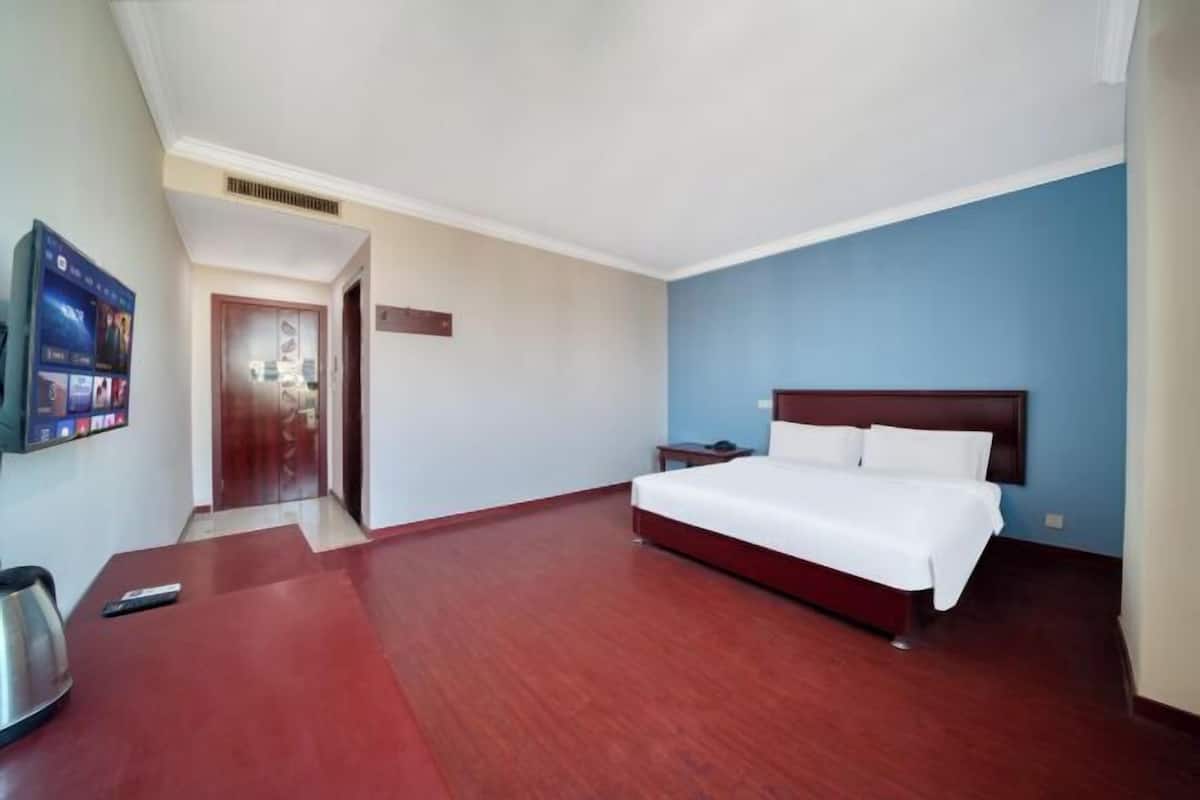 A hotel room with a wooden floor, a bed with white bedding, a TV on the wall, and a door leading to another room.