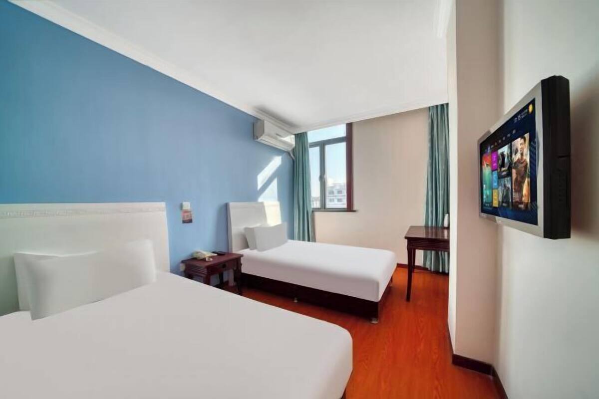 A hotel room with two beds, a TV on the wall, and a window with curtains.