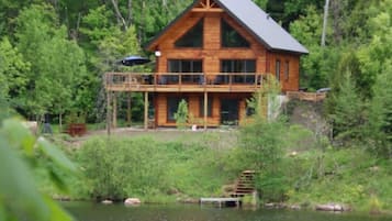 Une cabane en bois dotée d’un balcon donnant sur un lac, entourée d’une forêt dense.