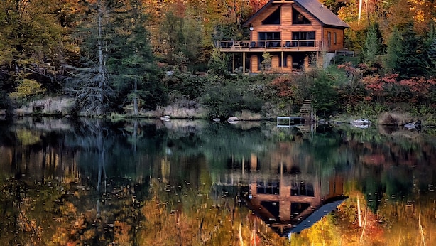 Eine Hütte am See mit Spiegelung, umgeben von Herbstlaub.