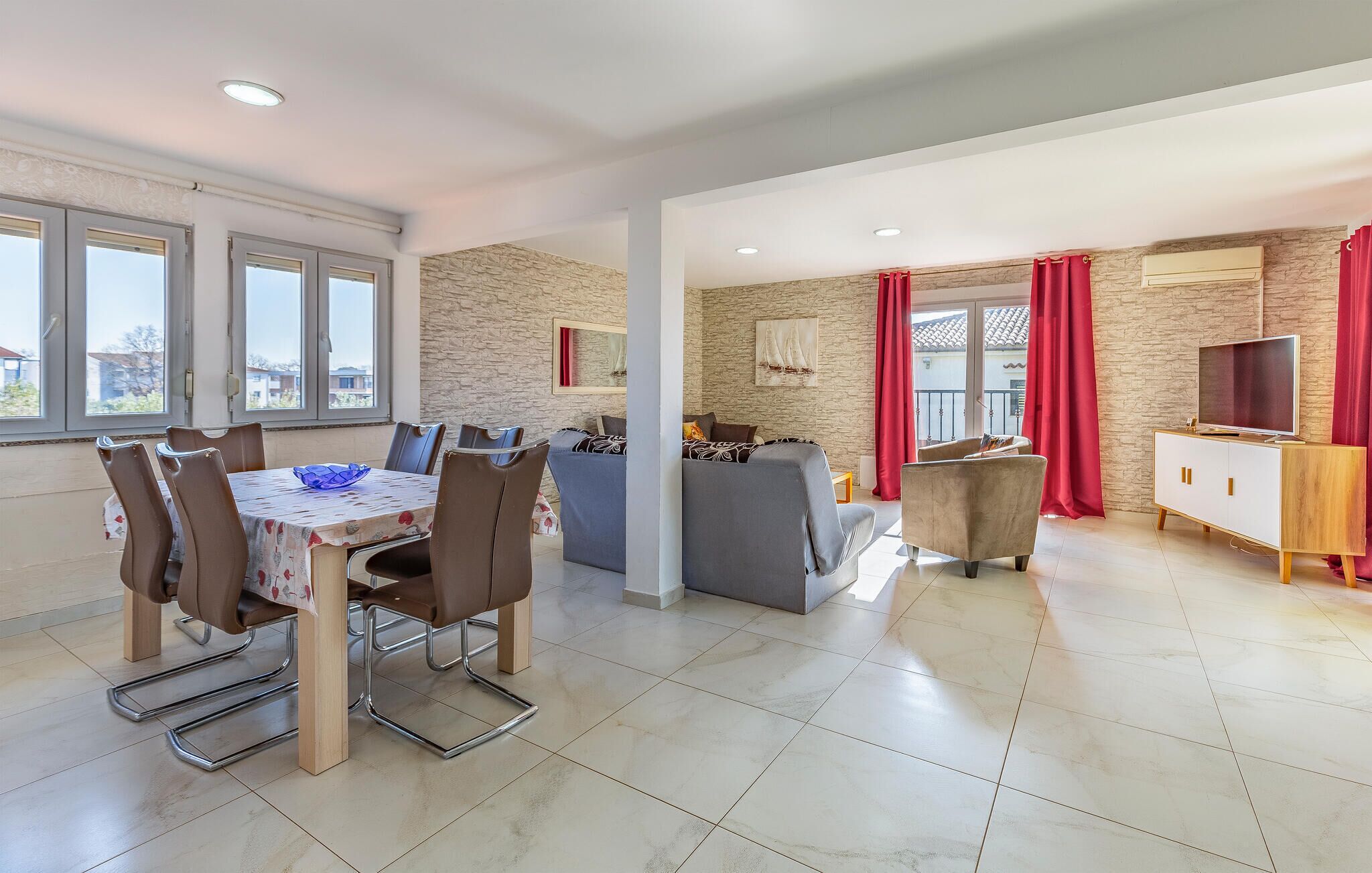 A spacious living area with a dining table, chairs, a sofa, and a TV.