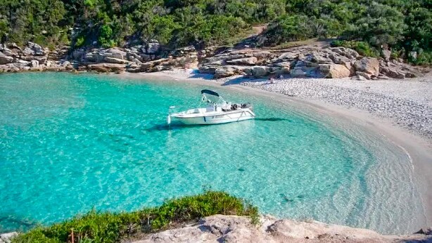 A boat on a clear turquoise sea with a rocky shoreline and greenery in the background. - Gorgeous home in OLETTA (OLETTA)