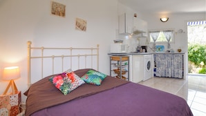 A bedroom with a bed, a bedside table, a lamp, and a view of a kitchen and balcony. - Gorgeous home in OLETTA (OLETTA)