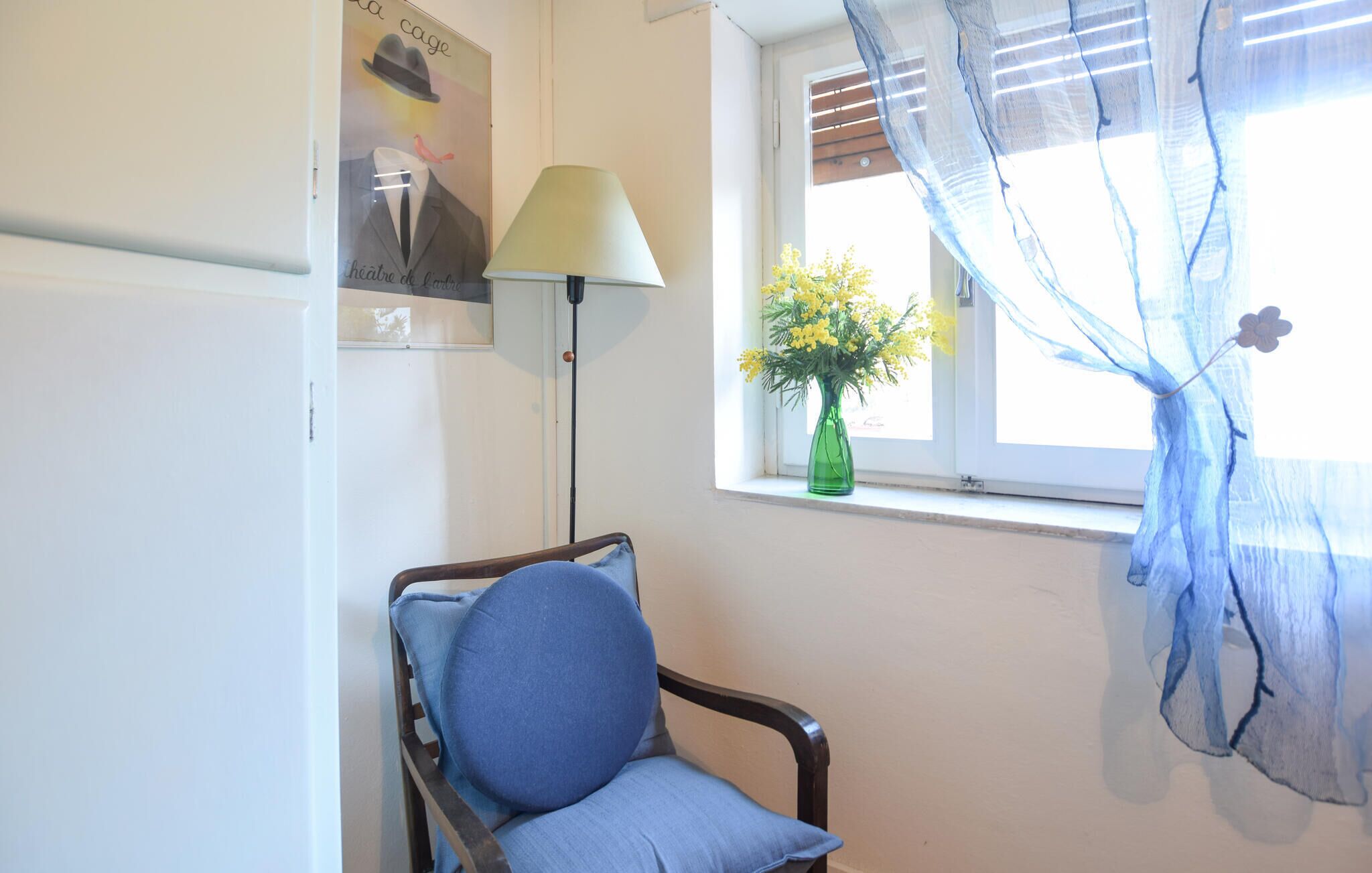A room with a chair, a lamp, a window with a curtain, and a poster on the wall.
