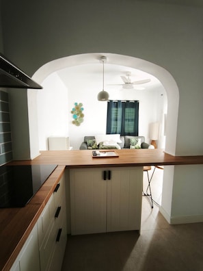 Una cocina moderna con encimera de madera, armarios blancos, ventilador de techo y un elemento decorativo en la pared.