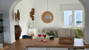 A modern kitchen with white cabinets, a wooden countertop, and a hanging light fixture. There is a wicker basket and a woven wall hanging on the wall.
