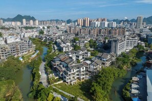 Un quartier résidentiel où se côtoient des bâtiments modernes et traditionnels, traversé par une rivière et bordé par des montagnes.