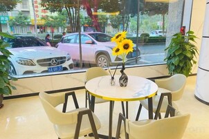 Interior de un hotel con una mesa redonda, cuatro sillas, un jarrón con girasoles y vistas a coches estacionados afuera.