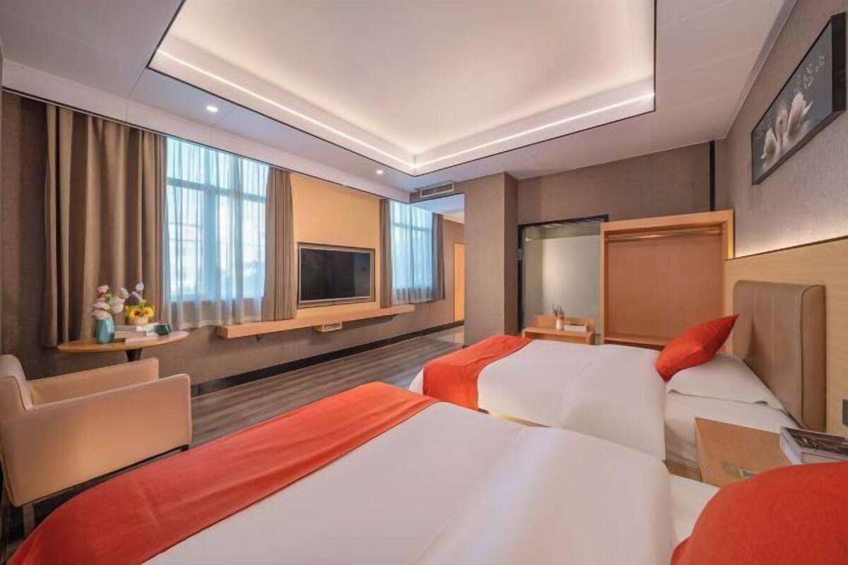 A hotel room with two beds, a TV, a desk, and a window with curtains.
