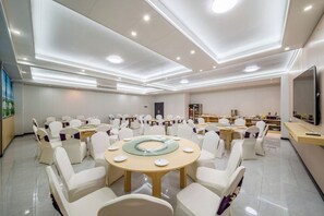 Une salle de conférence avec des tables rondes, des chaises blanches et un grand écran.