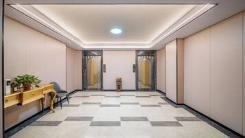 Un vestíbulo de hotel con una recepción, una planta, una zona de estar y una máquina de registro.