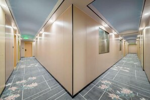 Un pasillo de hotel con techo plano, piso estampado y una puerta al final.