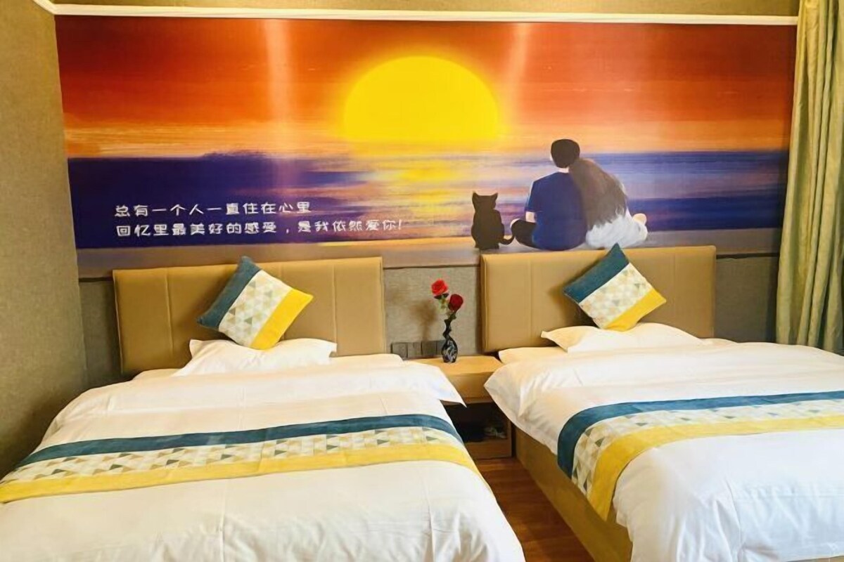 Une chambre d’hôtel avec deux lits, une fresque représentant un coucher de soleil sur le mur et un vase de fleurs sur la table de chevet.