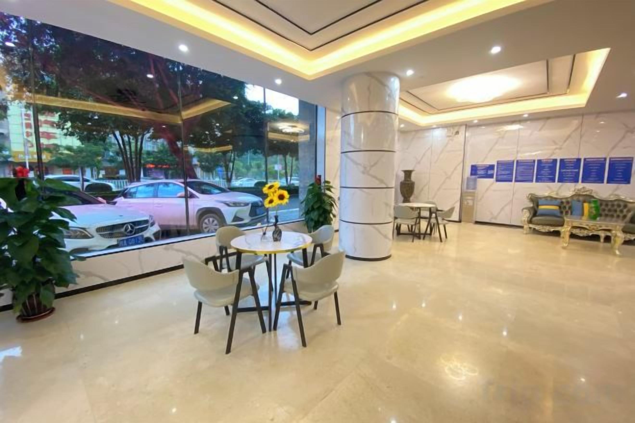 A hotel lobby with a marble floor, a reception desk, a seating area with chairs, and a large window with a view of parked cars and trees.