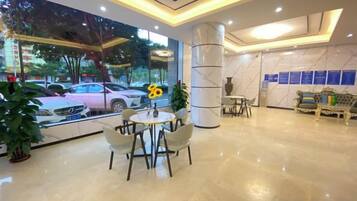 A hotel lobby with a marble floor, a reception desk, a seating area with chairs, and a large window with a view of parked cars and trees.