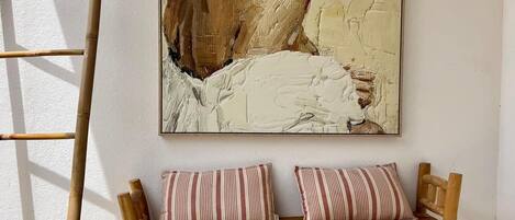 A wooden bench with striped cushions against a wall, a ladder leaning against the wall, and a large abstract painting above the bench.