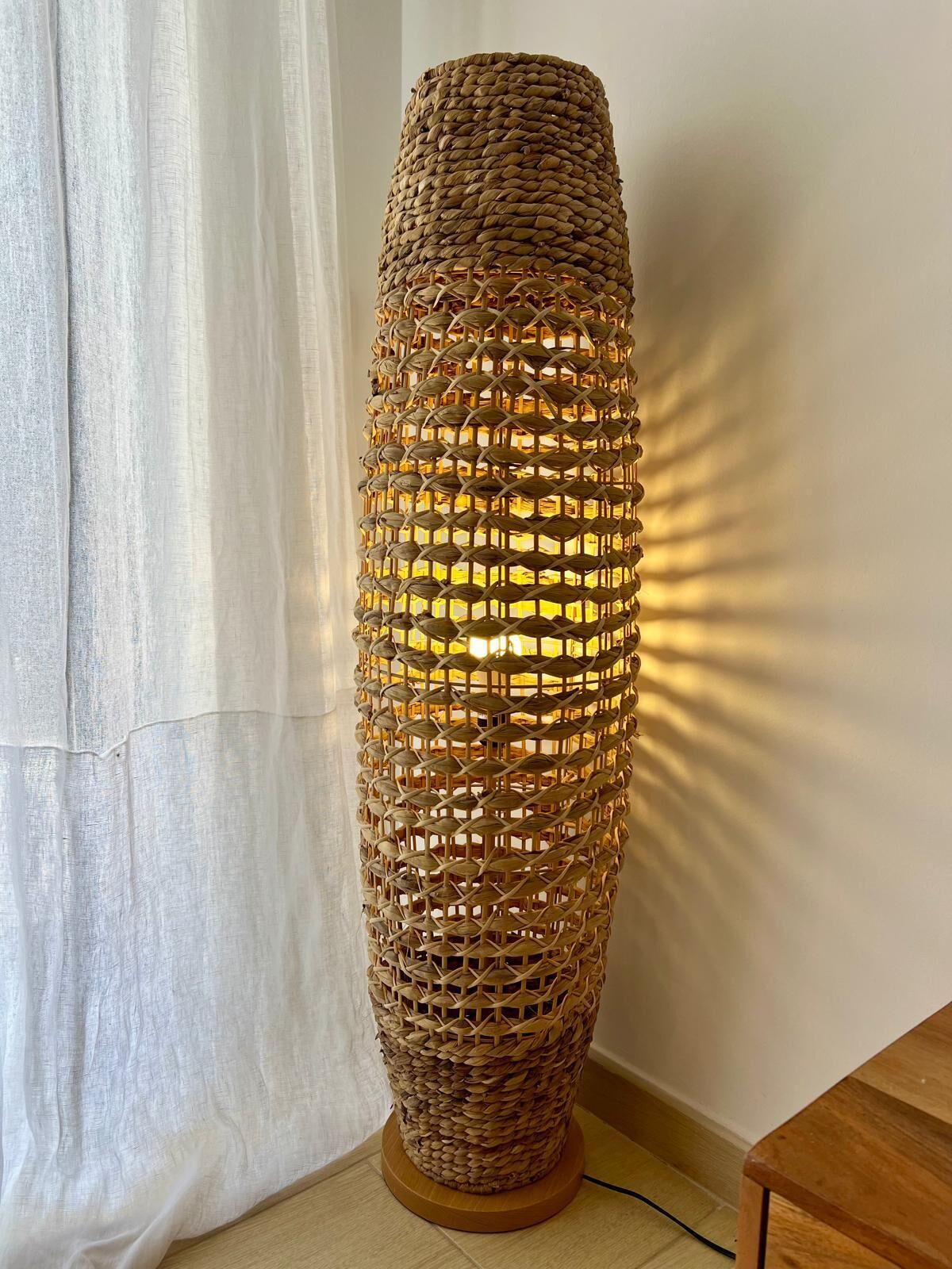 Una lámpara de pie alta, tejida, con forma cilíndrica y base de madera.