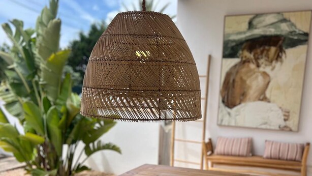 Una mesa de madera con una lámpara colgante de tela trenzada, un cuenco blanco y un cuadro en la pared.