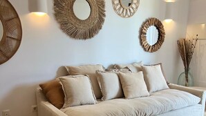 Un salón en tonos neutros con un sofá color beige, varios cojines y tres espejos colgados en la pared.