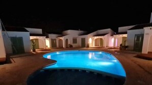 Ein Pool mit geschwungener Kante, umgeben von einem Gebäude mit mehreren Zimmern und einer überdachten Terrasse.