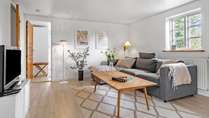 A modern living room with a wooden floor, a grey sofa, a wooden coffee table, and a TV stand.