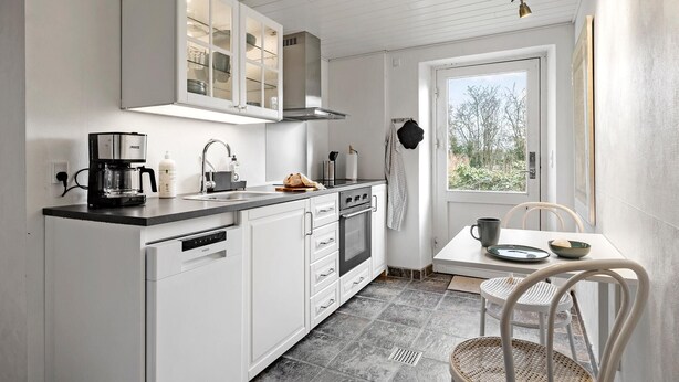 A compact kitchen with white cabinetry, a coffee maker, and a window providing a view of the outdoors.