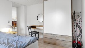 A bedroom with a bed, a desk, a chair, a wardrobe, and a vacuum cleaner.