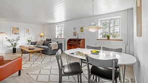 A modern living room with a dining area, white wooden ceiling, and large windows.