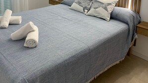 A neatly made bed with a blue bedspread and two pillows, a wooden slatted headboard, and a bedside table with a lamp. - Cales de Menorca 5, Cales de Menorca 5 - Cala Turqueta (Cala Blanca)
