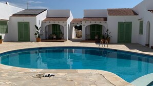 A swimming pool with stone tiles, white buildings with green shutters, and a clear sky. - Cales de Menorca 5, Cales de Menorca 5 - Cala Turqueta (Cala Blanca)