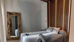 A modern bedroom with a large bed, a wooden-framed mirror, and a wall with vertical wooden slats. - Cales de Menorca 3, Cales de Menorca 3 - Cala Morell (Cala Blanca)