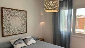 Une chambre à coucher comprenant un lit, un élément décoratif mural, un luminaire suspendu et une fenêtre avec des rideaux.