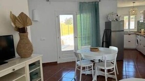 Une cuisine compacte comprenant un réfrigérateur, une table à manger avec des chaises et un téléviseur posé sur un meuble.