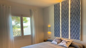 Ein Schlafzimmer mit einem großen Bett, einem Fenster mit Vorhängen, einer Wandleuchte und einer Wandverkleidung mit Muster.