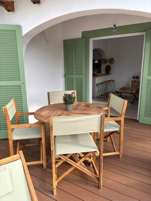 Um deck de madeira com uma mesa redonda e quatro cadeiras, um vaso de planta e uma porta verde com o número 3.